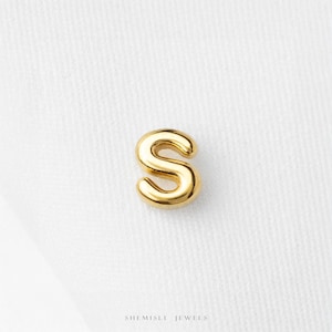 May include: A small, polished gold-tone letter S charm with a smooth, rounded surface. The letter features a classic serif-style font design with a reflective metallic finish. The text SHEMISLI JEWELS is printed in small black letters below the charm.