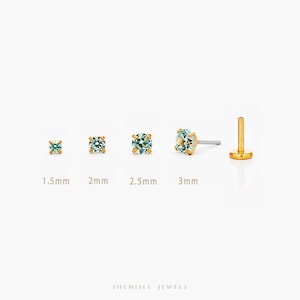 May include: A selection of gold stud earrings with light blue gemstones, varying in size from 1.5mm to 3mm. The earrings are presented on a white backdrop, highlighting their size differences. The brand name "SHEMISLI JEWELS" is at the bottom.