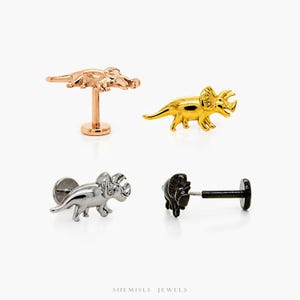 May include: Four dinosaur-shaped stud earrings in rose gold, gold, silver, and black. The earrings are displayed on a white background. The brand name "SHEMISLI JEWELS" is at the bottom.