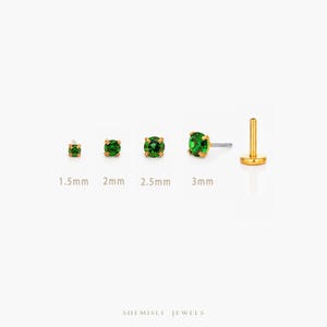 May include: A selection of gold stud earrings featuring bright green gemstones. The earrings are displayed in various sizes, with the gemstones measuring 1.5mm, 2mm, 2.5mm, and 3mm. A single gold post earring is also shown. The text "SHEMISLI JEWELS" is at the bottom.