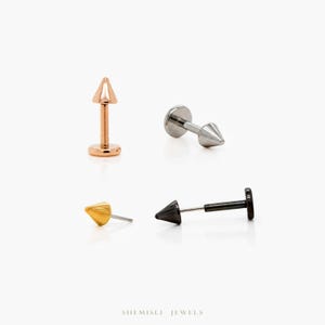 May include: Four lip piercing studs in rose gold, silver, gold, and black. Each stud has a conical spike design. The studs are displayed on a white background. The text "SHEMISLI JEWELS" is at the bottom.