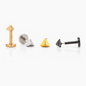 Peut inclure: Présentation de quatre piercings pour lèvres ou cartilage. Les clous présentent un sommet triangulaire en or, argent et noir. Les tiges sont en métal argenté et noir. Les clous sont présentés sur fond blanc.