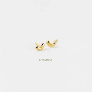 Peut inclure: Une paire de boucles d'oreilles à clous dorées en forme de cœur. Les boucles d'oreilles sont sur fond blanc. Le nom de la marque "SHEMISLI" est imprimé en dessous.
