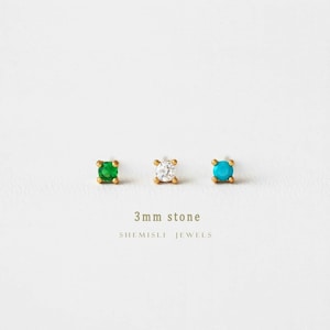 May include: Three gold stud earrings with 3mm stones in green, clear, and turquoise. The earrings are displayed on a white background. The text "3mm stone" and "SHEMISLI JEWELS" are below the earrings.