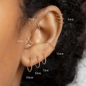 May include: An ear displaying several gold hoop earrings of varying sizes. The earrings are 6 mm, 7 mm, 8 mm, 10 mm, and 12 mm in diameter. The hoops feature a twisted rope design, adding texture to the jewellery.