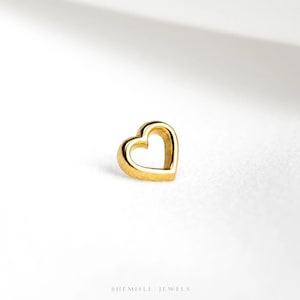 May include: A small, gold heart-shaped piece of jewellery. The heart is a solid outline with a smooth, polished finish. The jewellery is set against a white background, with the brand name "SHEMISLI JEWELS" at the bottom.