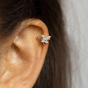 May include: A gold ear cuff with a butterfly design, adorned with clear crystals. The cuff is attached with a small ball stud. The jewellery is designed to be worn on the upper ear cartilage.