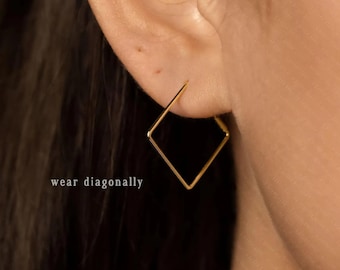 May include: A close-up of a gold-coloured square earring worn on an ear. The earring is a simple, geometric design, with a square shape. The text "wear diagonally" is visible in the image.