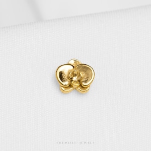 May include: A gold-coloured orchid flower pendant. The pendant is a detailed, three-dimensional representation of an orchid, with curved petals and intricate detailing. The jewellery is set against a white background.