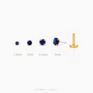 May include: A selection of gold stud earrings featuring deep blue gemstones. The earrings are shown in sizes 1.5mm, 2mm, 2.5mm, and 3mm. A single earring post is also visible. The brand name "SHEMISLI JEWELS" is at the bottom of the image.