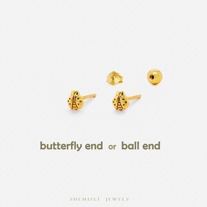 May include: Gold-coloured ladybird stud earrings with a butterfly back and a ball back option. The earrings have a detailed design and are displayed on a white background. The text "butterfly end or ball end" is below the earrings.