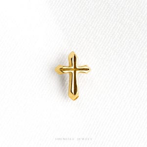 May include: A small, polished gold cross pendant featuring a central vertical ridge and pointed ends on each arm. The cross has a smooth, reflective metallic finish and is centred on a plain white background with the text SHEMISLI JEWELS below.