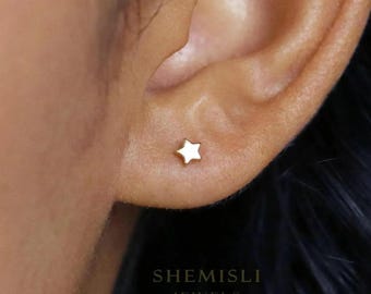 Könnte beinhalten: Ein kleiner, goldfarbener Ohrstecker in Sternform ist im Ohr einer Person zu sehen. Der Ohrring hat ein schlichtes, minimalistisches Design. Der Text "SHEMISLI JEWELS" ist unten im Bild aufgedruckt.