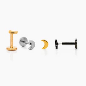 May include: Four pieces of body jewellery, each featuring a crescent moon design. The pieces are in gold, silver, and black. The jewellery is designed for lip or ear piercings. The pieces are displayed on a white background.