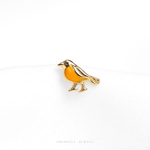 May include: A gold-coloured bird-shaped pin with an orange breast and black eye. The bird is standing on a white surface. The pin is a jewellery item. The brand name "SHEMISLI JEWELS" is printed at the bottom of the image.