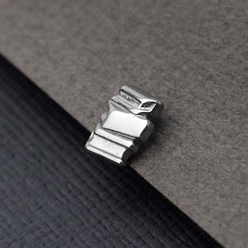 A close-up image of a small, metallic object, possibly a piece of jewelry, resting on a textured gray surface.