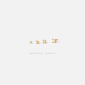 May include: Four gold stud earrings with opal stones are displayed against a white backdrop. The earrings are of varying sizes, with the largest being square. The brand name "SHEMISLI JEWELS" is printed in a serif font below the earrings.