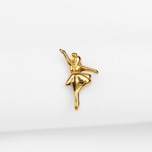 May include: A small, gold-coloured ballerina figurine in a graceful pose, with one arm raised and the other extended. The dancer is wearing a tutu. The figurine is set against a plain white background.