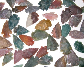 May include: A collection of arrowheads made from various types of agate. The arrowheads are all different shapes and sizes, and they are all a variety of colors, including green, brown, red, and white.