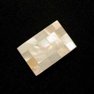 May include: A rectangular white mother of pearl inlay with a checkered pattern.