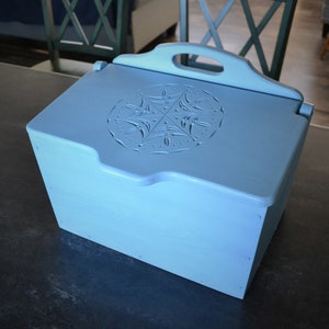 May include: A light blue wooden bread box with a carved design on the lid and a handle on top.