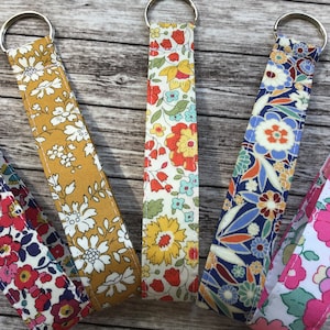 May include: Five colourful fabric keychains with floral patterns. The keychains are made of a soft, woven fabric and feature a silver metal ring.