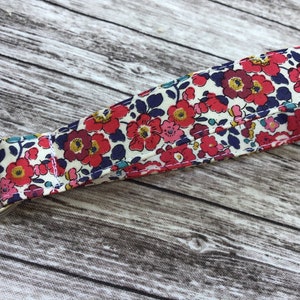 Puede incluir: Un llavero de tela blanca con un patr&oacute;n floral en tonos rojos, rosas, azules y amarillos. El llavero tiene un anillo de metal plateado.