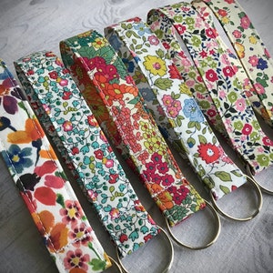 Puede incluir: Un conjunto de seis llaveros coloridos con patrones florales. Cada llavero tiene un anillo de metal plateado. Los llaveros están hechos de tela y tienen un fondo blanco con flores de varios colores.