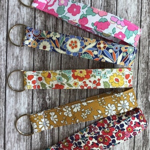 Puede incluir: Cinco llaveros coloridos con patrones florales. Cada llavero tiene un anillo de metal plateado y est&aacute; hecho de tela con una variedad de estampados florales.