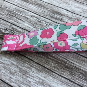 Puede incluir: Un llavero de tela blanca con un estampado floral rosa. El llavero tiene un anillo de metal plateado.
