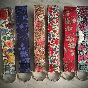 May include: Six colourful keychains with floral patterns. The keychains are made of fabric and have silver metal rings.