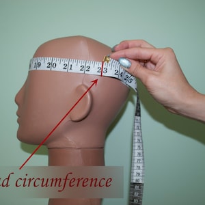 May include: A white measuring tape is wrapped around a mannequin's head to measure the head circumference. The tape reads "19 20 21 22 23 24 25" and "head circumference".