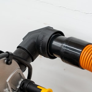 May include: Black dust collection adapter with a 90-degree angle, connected to an orange hose. The adapter has the text "inspire woodworking" printed on it.