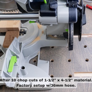 May include: A close-up of a gray and green power saw with a wood block in the blade. The saw is on a gray surface with holes. The text "After 10 chop cuts of 1-1/2" x 4-1/2" material. Factory setup w/36mm hose." is below the saw.