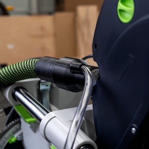 May include: Close-up of a black and green power tool with a green hose attached. The tool has a black and silver handle and a black and green label that reads "FESTOOL KS 120 EB-Plus".