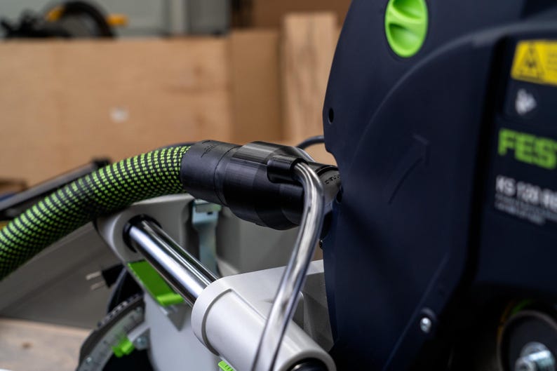 May include: Close-up of a black and green power tool with a green hose attached. The tool has a black and silver handle and a black and green label that reads "FESTOOL KS 120 EB-Plus".
