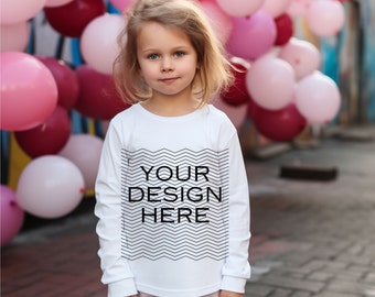 Puede incluir: Una niña lleva una camiseta blanca de manga larga con el texto "YOUR DESIGN HERE" en negro. La camiseta tiene un diseño de zigzag negro. Globos rosas y granates se ven en el fondo.