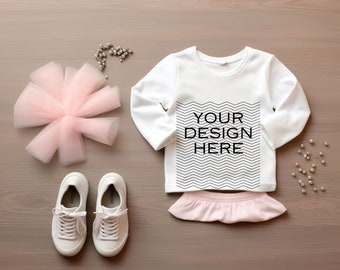Puede incluir: Camiseta blanca de manga larga con el texto "YOUR DESIGN HERE" en negro. La camiseta tiene una falda rosa con volantes y zapatillas blancas.