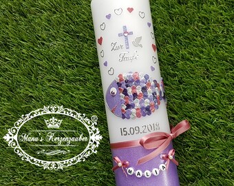 May include: A white baptism candle with a purple and silver fish design, hearts, and a cross. The candle has the text "Zur Taufe" and the date "15.09.2018". A pink ribbon and the name "MALIA" are also featured.