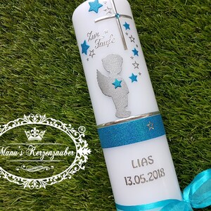 Puede incluir: Vela de bautismo blanca con un diseño de ángel azul y plateado. La vela tiene una banda de purpurina azul y el nombre "LIAS" y la fecha "13.05.2018" están inscritos en la vela.