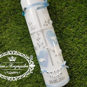 Puede incluir: Una vela de bautizo blanca decorada con detalles azules, adornos plateados y el texto "Zur Taufe". Presenta dos diseños en forma de corazón azul con una paloma y un pez. También se muestra el nombre "Mateo Elio" y la fecha "20.05.2017".