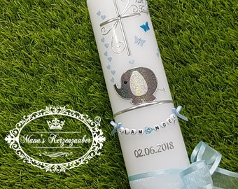 Può includere: Una candela bianca decorata con una croce argentata, farfalle blu e cuori. Presenta un design a elefante glitterato e il nome "Liam Noel" con la data 02.06.2018. Un nastro e un fiocco blu completano il design.