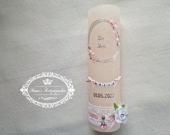 May include: A light pink candle decorated with a silver floral design and the words "Zur Taufe". The candle is adorned with a banner spelling "MAILA" and the date 01.05.2022. A white lace and pink ribbon complete the design.