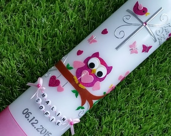 Può includere: Una candela bianca decorata con abbellimenti rosa e argento. La candela presenta un gufo, farfalle, cuori e una croce. Sono presenti anche il nome "Malin Sofie" e la data "06.12.2015". Un nastro rosa è legato alla base.