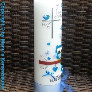 Peut inclure: Une bougie blanche d&eacute;cor&eacute;e d'oiseaux, de papillons et de c&oelig;urs bleus. Un ruban et un n&oelig;ud bleus sont attach&eacute;s autour de la base. La bougie porte la date "14.08.20".