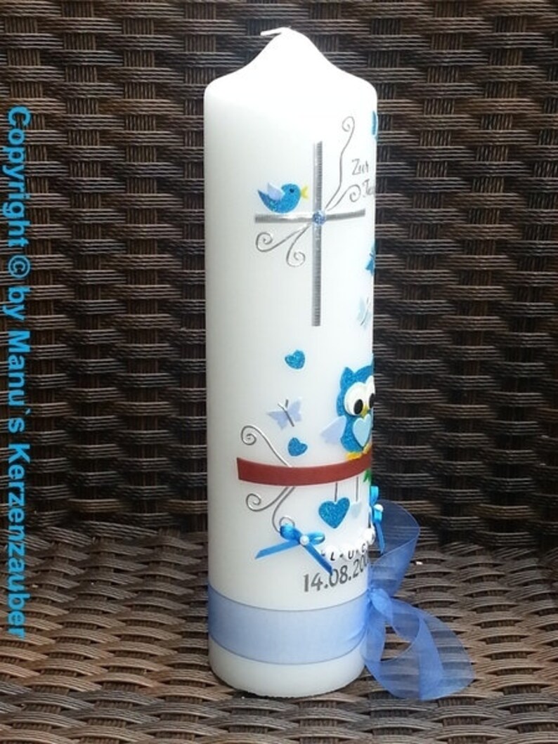 Peut inclure: Une bougie blanche d&eacute;cor&eacute;e d'oiseaux, de papillons et de c&oelig;urs bleus. Un ruban et un n&oelig;ud bleus sont attach&eacute;s autour de la base. La bougie porte la date "14.08.20".