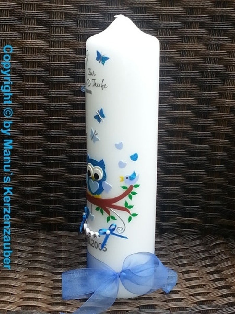 Peut inclure: Une bougie blanche d&eacute;cor&eacute;e de papillons bleus, d'un hibou et d'un oiseau perch&eacute; sur une branche. La bougie a un ruban bleu et le texte "Zur Taufe" et l'ann&eacute;e 2005.