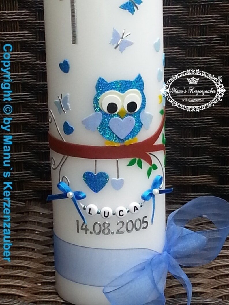 Peut inclure: Une bougie blanche d&eacute;cor&eacute;e d'un hibou bleu, de papillons et de c&oelig;urs. Le nom "LUCA" et la date "14.08.2005" sont affich&eacute;s. Un ruban et un n&oelig;ud bleus ajoutent une touche d&eacute;corative. La bougie est un article personnalis&eacute;.