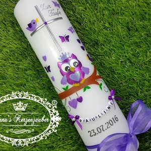 Puede incluir: Vela blanca decorada con un búho morado, mariposas y corazones. La vela tiene una cruz, el texto "Zur Taufe" y el nombre "Pauline" con la fecha "23.07.2016". Una cinta morada está atada a la base.