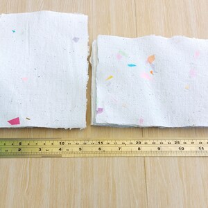 May include: Two stacks of handmade paper with colorful flecks. The paper is white and has a rough texture. A ruler is placed below the paper, measuring 12 inches.